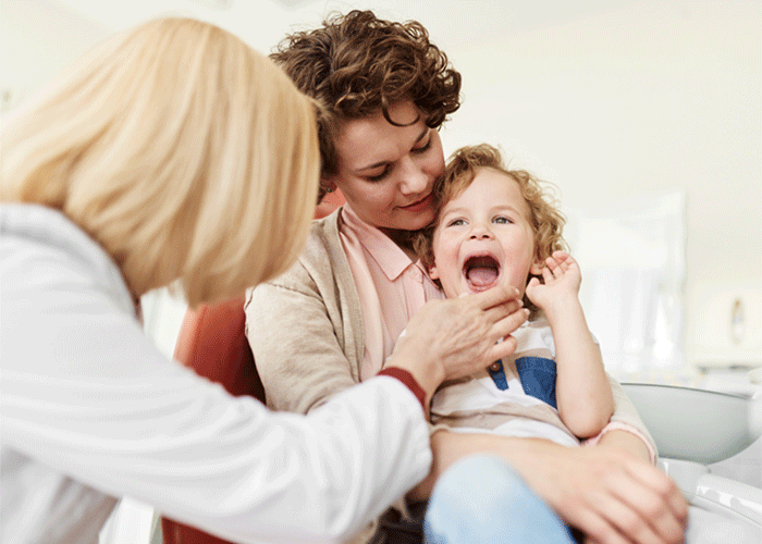 mother holding her child while a doctor examines the child's mouth